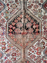 an antique qashqai rug with a cream field and red, pink and blue accents