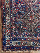 an antique qashqai rug with a dark field and blue, red and ivory accents