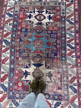 an antique caucasian rug with red and blue accents and a large geometric pattern
