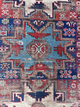 an antique caucasian rug with red and blue accents and a large geometric pattern