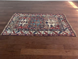 an antique caucasian rug with red and blue accents and a large geometric pattern
