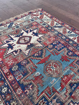 an antique caucasian rug with red and blue accents and a large geometric pattern