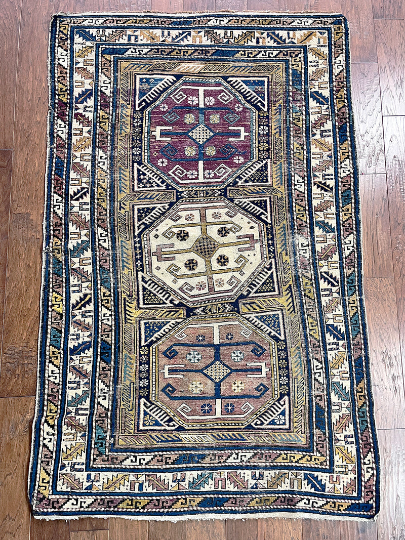 an antique caucasian shirwan rug with lilac, yellow and blue accents and a large cream medallion