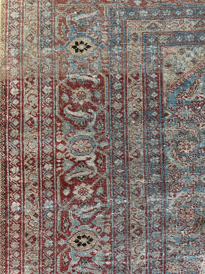 an antique tabriz rug with a teal field, red border and a delicate floral pattern