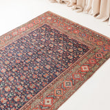 Decorative rug with intricate patterns on a white floor, with beige curtains in the background.