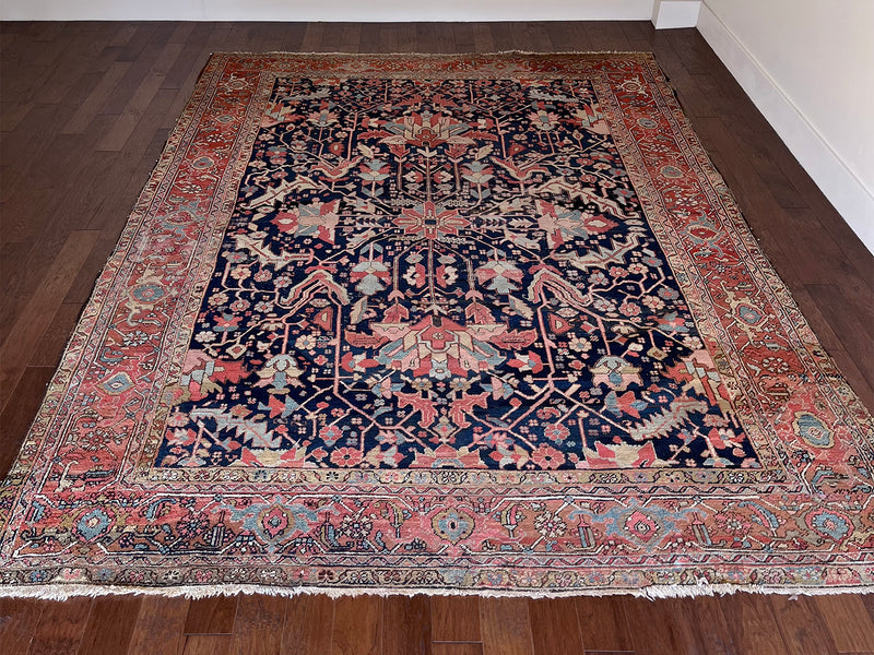 a large antique heriz rug with a dark blue field and a bright coral and pink border
