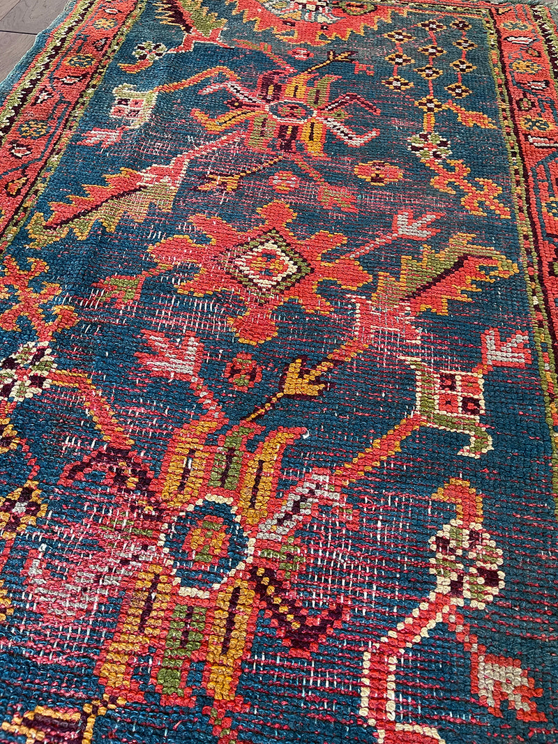 an antique oushak rug with a dark blue field and a red, orange and lime green pattern