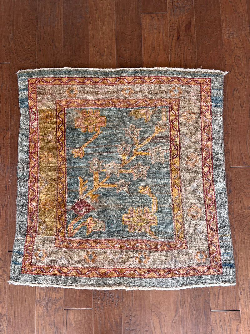 a mini antique oushak rug with a blue field, a floral pattern and a taupe and lime green border