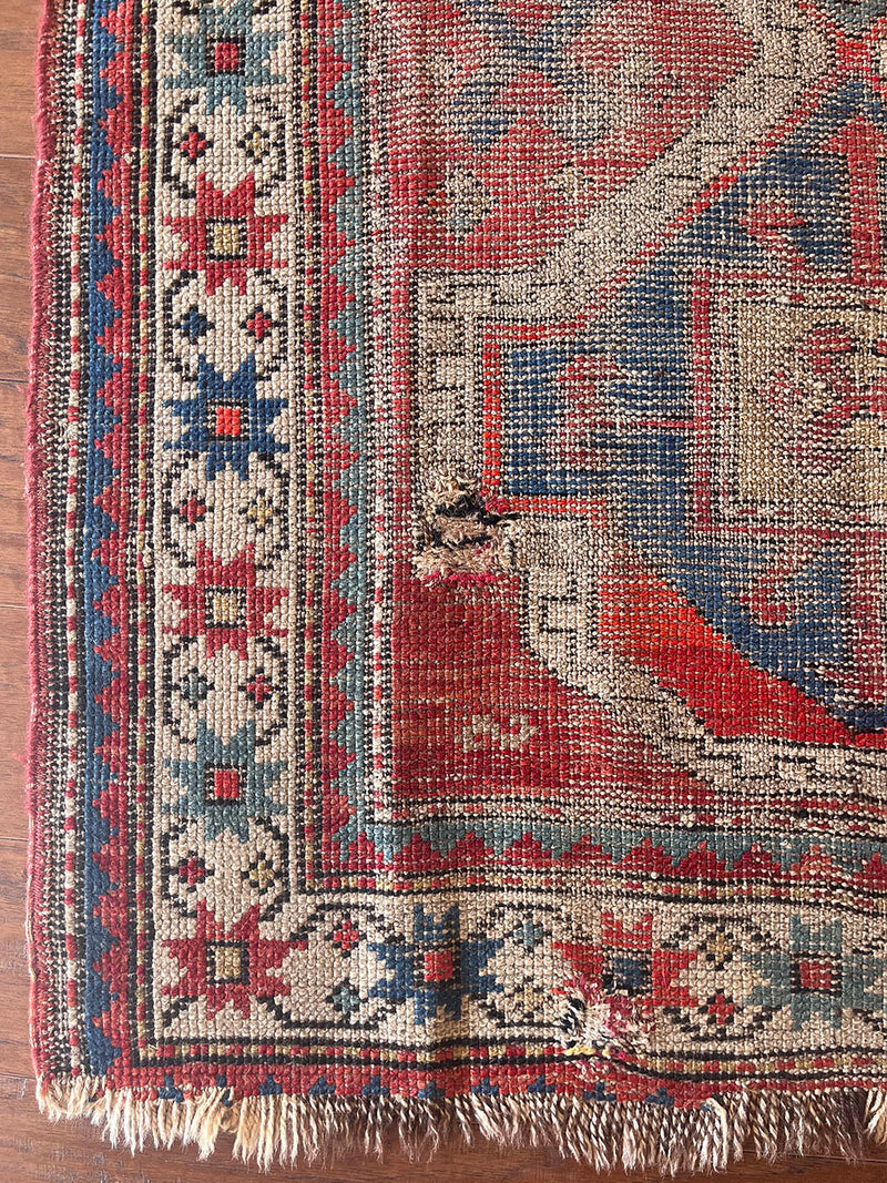 an antique caucasian rug with a rusty red field and blue medallions