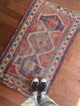 an antique caucasian rug with a rusty red field and blue medallions