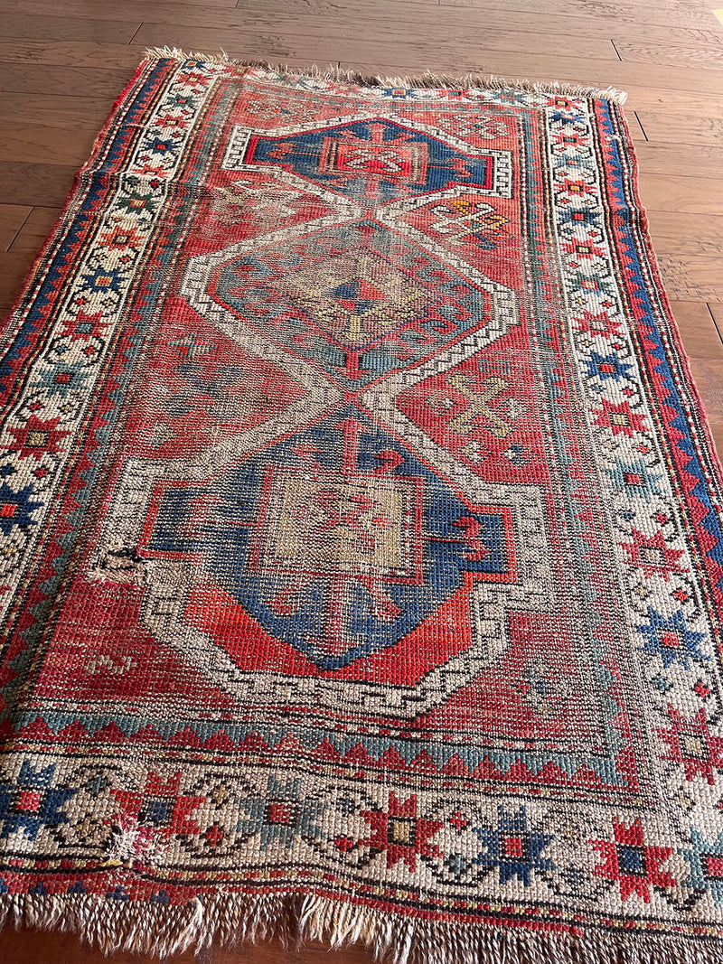 an antique caucasian rug with a rusty red field and blue medallions