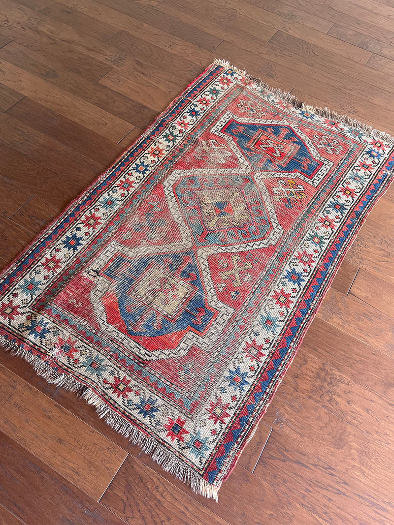 an antique caucasian rug with a rusty red field and blue medallions