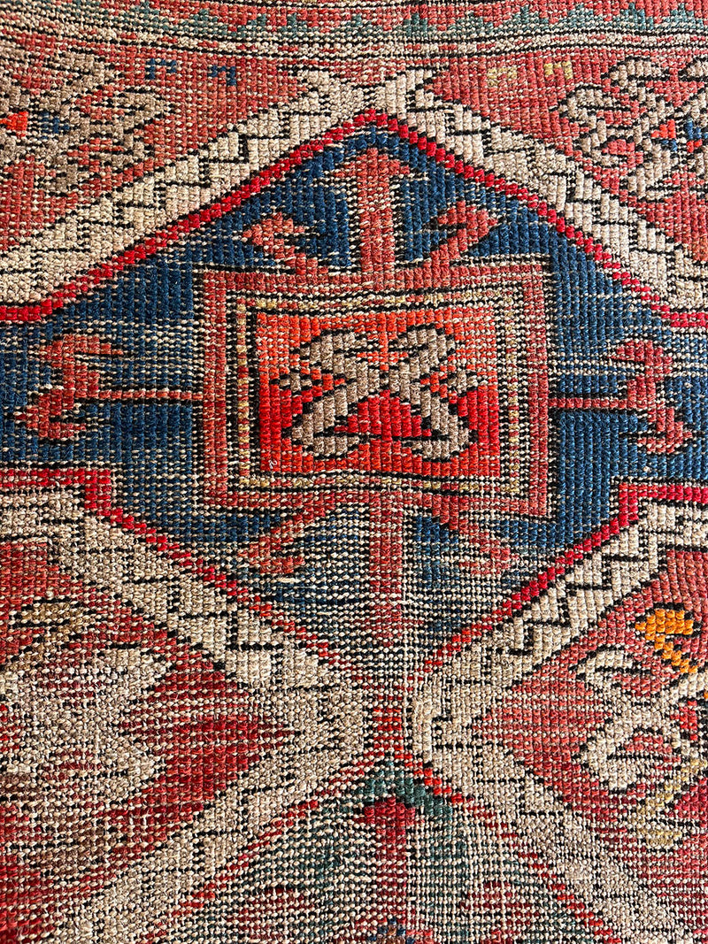 an antique caucasian rug with a rusty red field and blue medallions