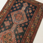 A traditional Persian-style area rug with a dark navy blue field, featuring large central medallions in rust red, beige, and orange, surrounded by a patterned border.