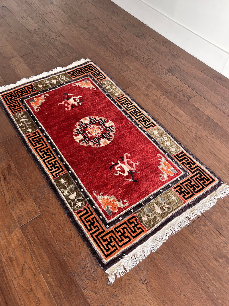 a vintage tibetan meditation rug with a solid raspberry red field and a pretty lilac and sage border in a geometric and floral design