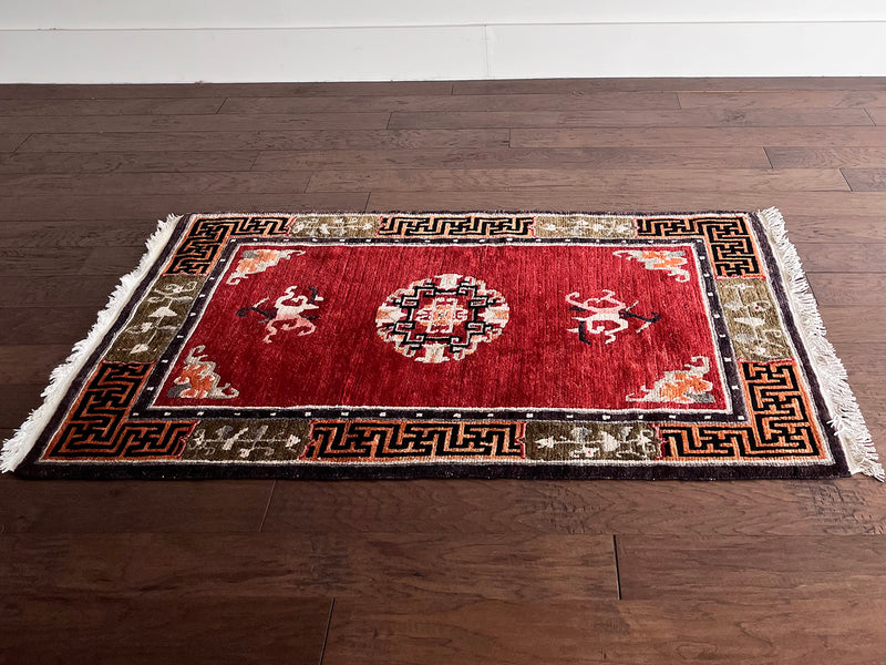 a vintage tibetan meditation rug with a solid raspberry red field and a pretty lilac and sage border in a geometric and floral design