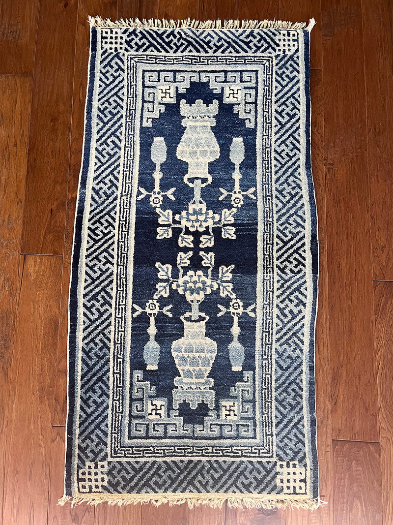 an antique chinese peking rug with a solid blue field and traditional chinese jar design in light blue and cream