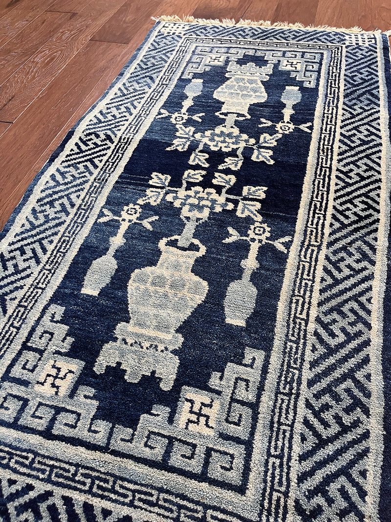 an antique chinese peking rug with a solid blue field and traditional chinese jar design in light blue and cream