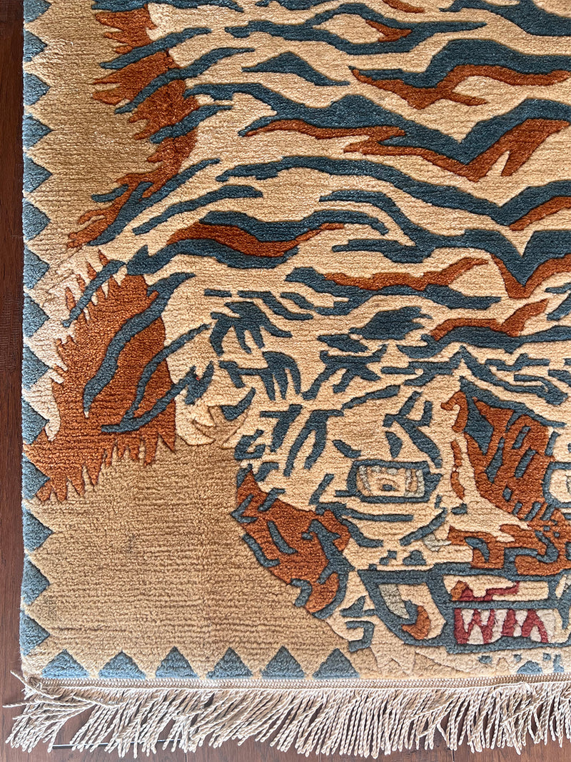 a vintage chinese rug with a large graphic tiger design in blue and burnt orange stripes