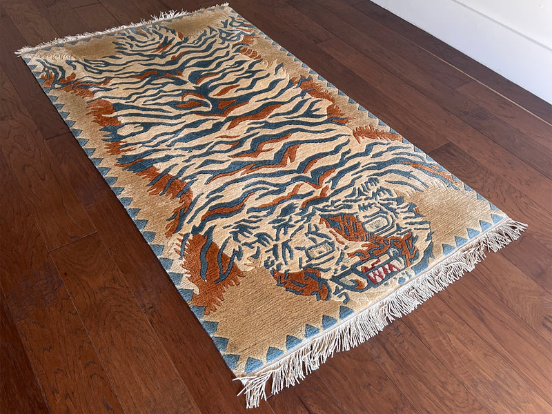 a vintage chinese rug with a large graphic tiger design in blue and burnt orange stripes