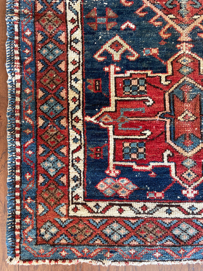 a mini antique heriz rug with a dark blue abrash field and red medallions
