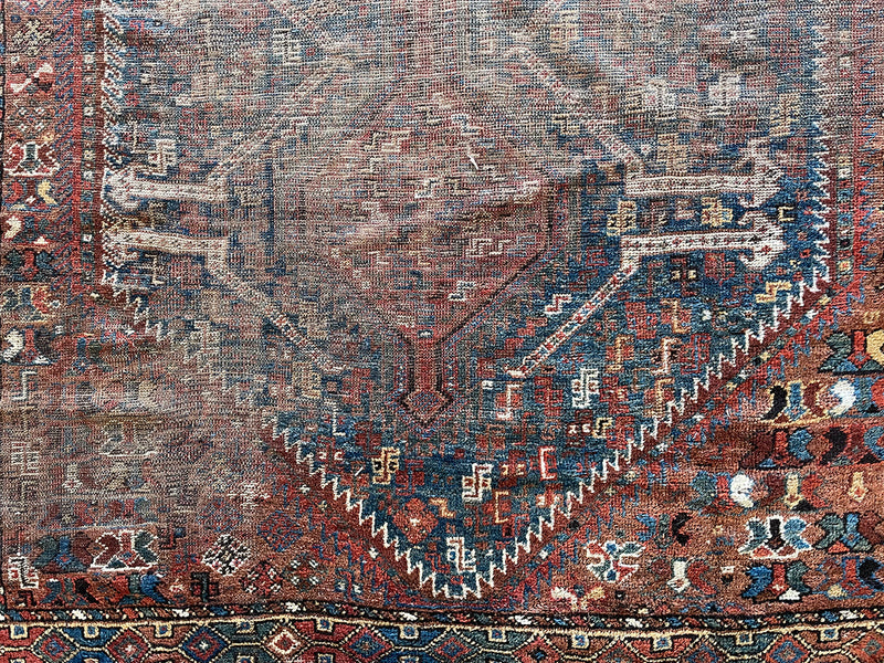 an antique shiraz rug with earthy tones in teal blue and mud red tones