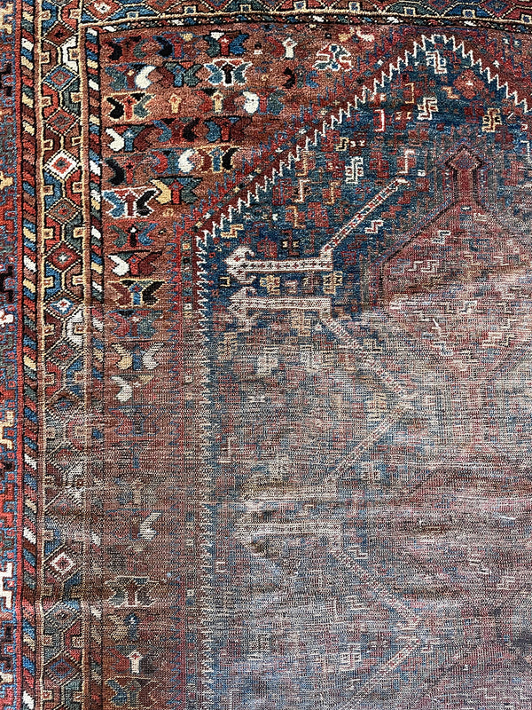 an antique shiraz rug with earthy tones in teal blue and mud red tones