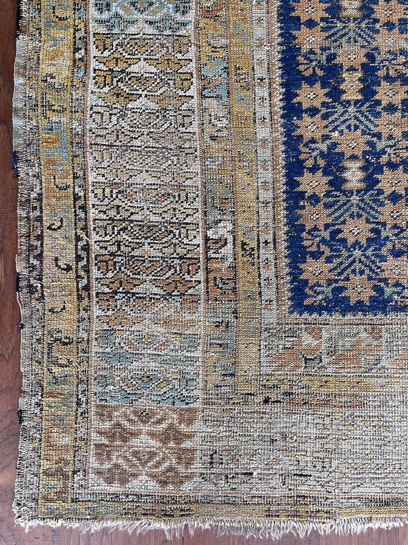 an antique kula rug with a blue field, a star pattern and a mustard yellow border