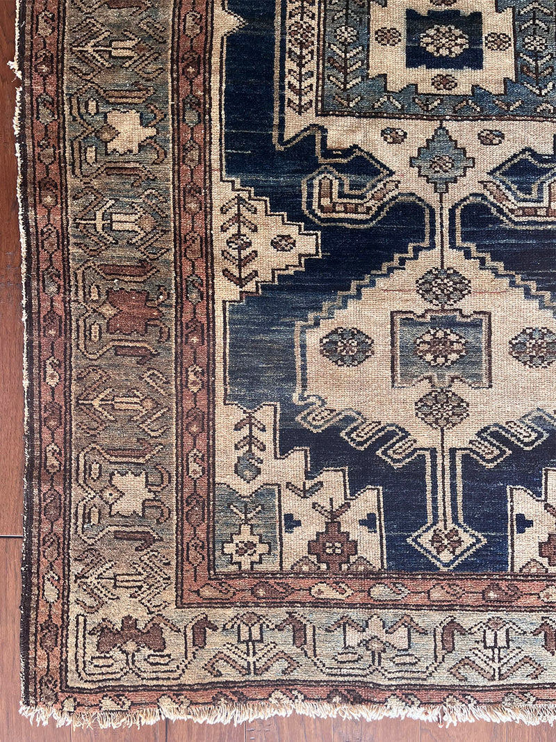 an antique malayer rug with a dark blue field, a large taupe medallion and a lilac border