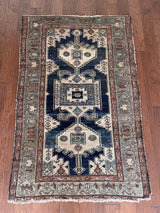 an antique malayer rug with a dark blue field, a large taupe medallion and a lilac border