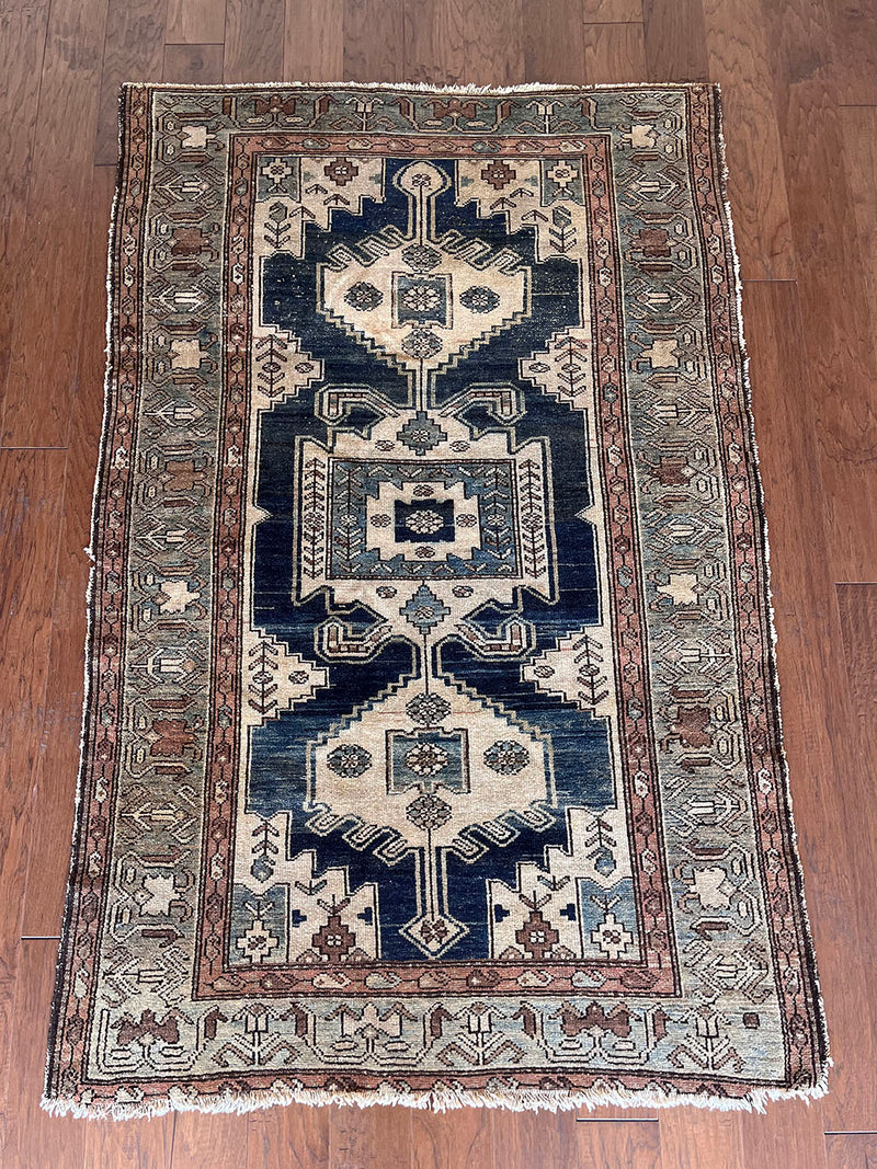 an antique malayer rug with a dark blue field, a large taupe medallion and a lilac border