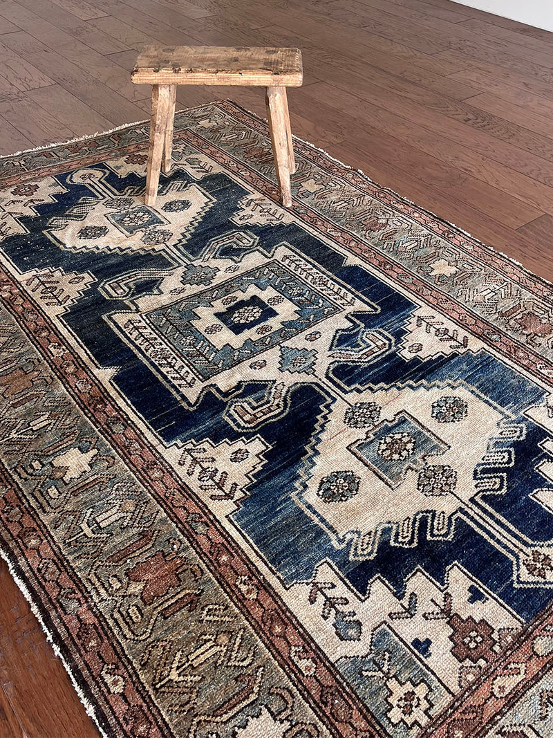 an antique malayer rug with a dark blue field, a large taupe medallion and a lilac border