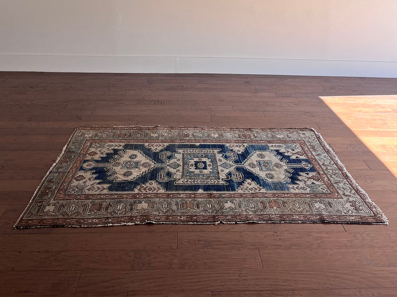 an antique malayer rug with a dark blue field, a large taupe medallion and a lilac border