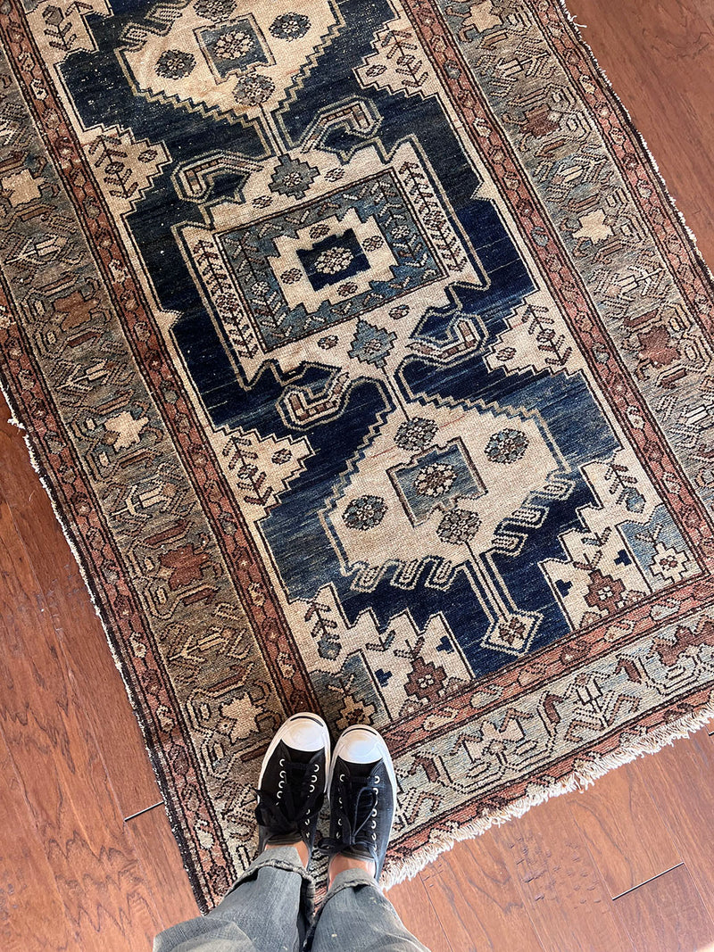 an antique malayer rug with a dark blue field, a large taupe medallion and a lilac border