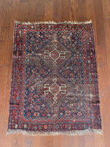 an antique qashqai rug with a dark blue field and a brown/red medallion and border