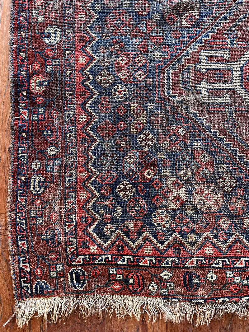 an antique qashqai rug with a dark blue field and a brown/red medallion and border