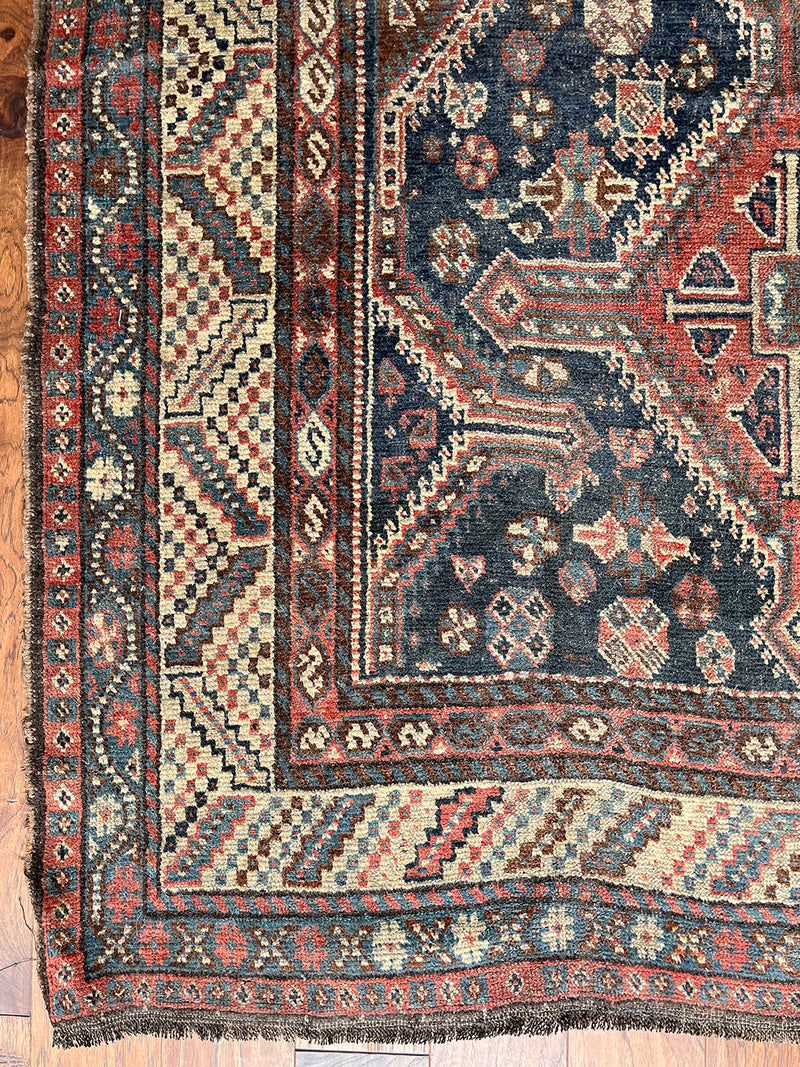 an antique qashqai rug with a dark blue field and brick red central medallions