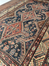 an antique qashqai rug with a dark blue field and brick red central medallions