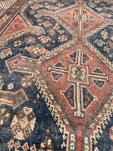 an antique qashqai rug with a dark blue field and brick red central medallions