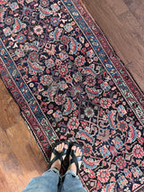 am antique heriz runner with a near black field and a pink and blue floral pattern