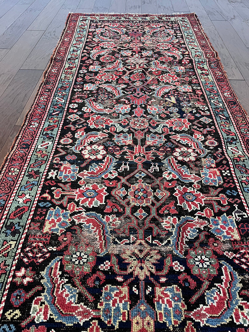 am antique heriz runner with a near black field and a pink and blue floral pattern