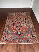 a large antique heriz rug with pink, coral, blue and green accents and a large navy blue medallion