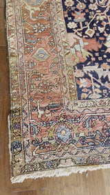 a large antique heriz rug with a dark blue field and a bright coral and pink border