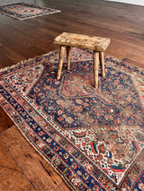 a small antique qashqai rug with a dark blue field, cream corners and red accents
