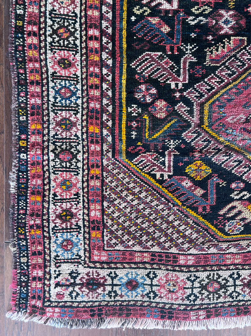 a vintage qashqai rug with a dark blue field and hot pink and yellow accents