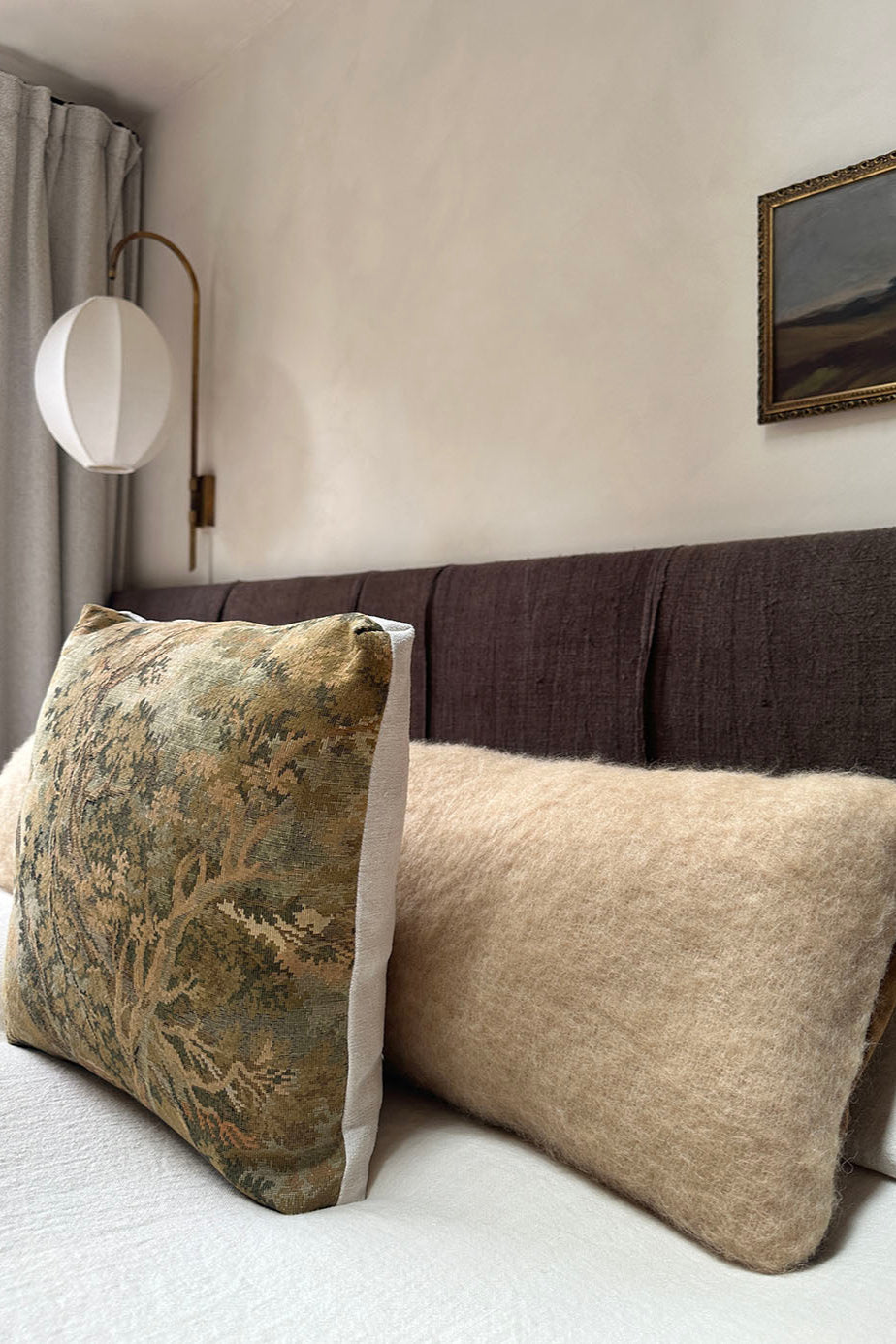 Decorative pillows on a bed with a lamp and painting in the background