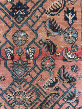an antique bakshaish rug with a salmon pink field and green and teal floral pattern