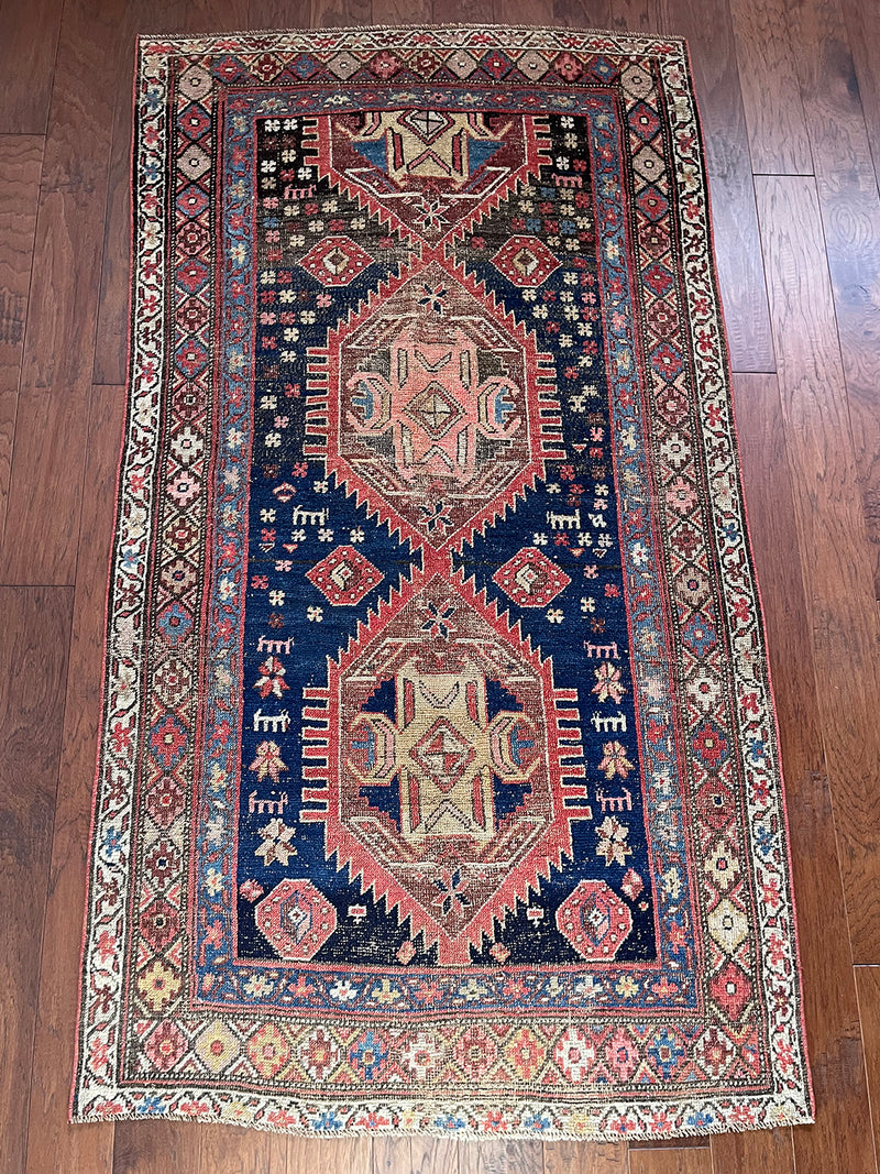 an antique kurdish rug with a blue field and coral and yellow accents in a geometric pattern
