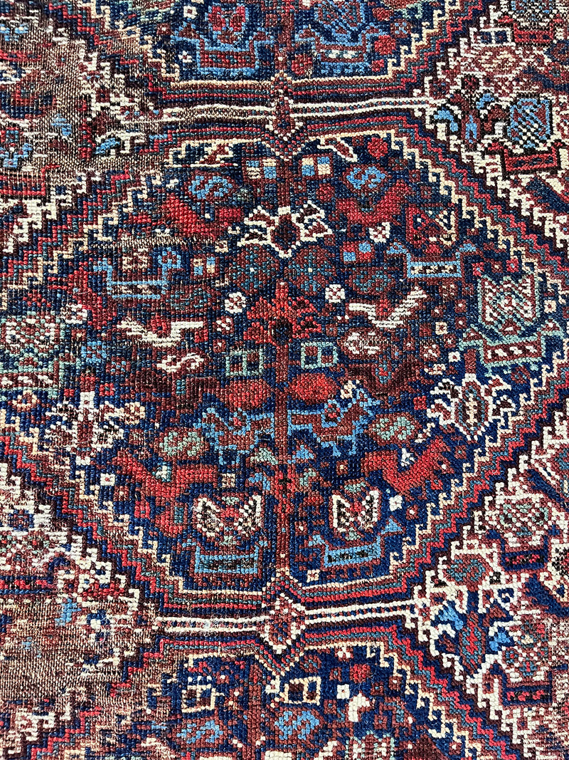 an antique qashqai rug with a dark field and blue, red and ivory accents