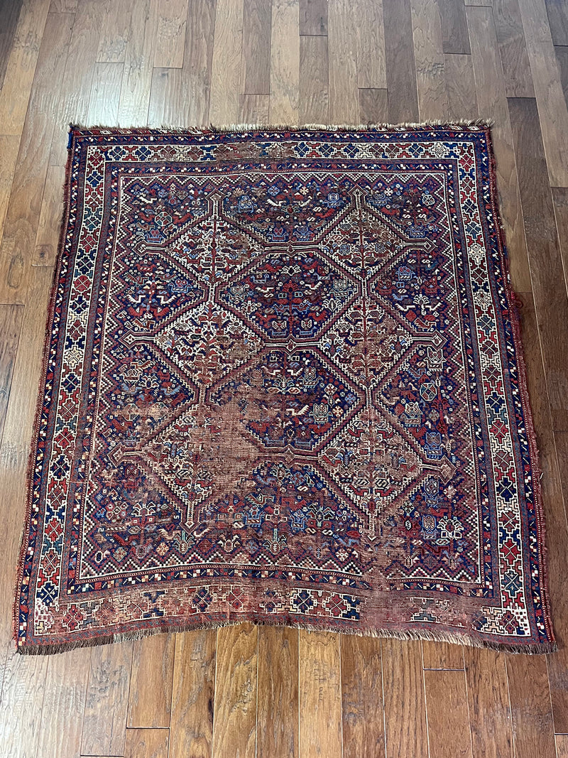 an antique qashqai rug with a dark field and blue, red and ivory accents